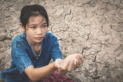 High angle view of girl sitting with hands cupped on cracked field