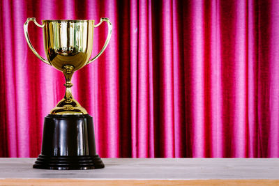 Close-up of trophy on wooden table against curtain