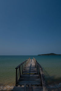 Pier over sea against clear blue sky