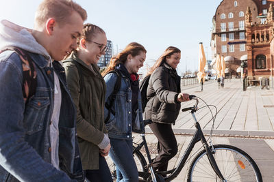 Side view of friends walking with teenage girl holding bicycle in city