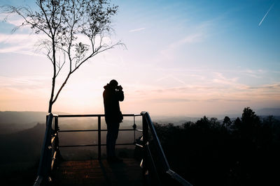 Silhouette man photographing on observation point against sky during sunset