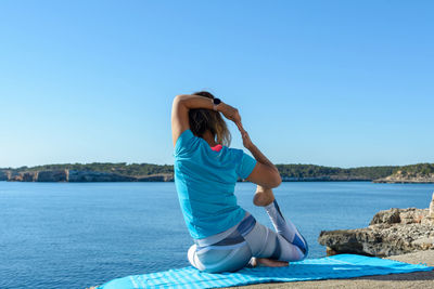 Middle-aged fitness woman outdoors in front of the sea does yoga stretching exercises