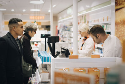 Customers and pharmacists standing at checkout in medical store