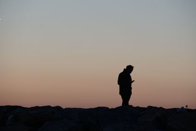 Silhouette man standing on rock against sky