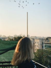 Rear view of woman looking at cityscape against sky