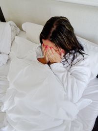 High angle view of woman covering face on bed at home