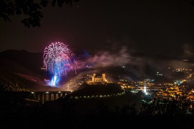 Firework display over illuminated city against sky at night