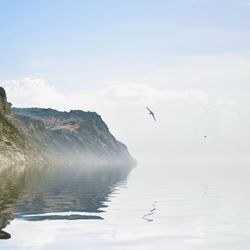 Scenic view of sea by cliff against sky during foggy weather