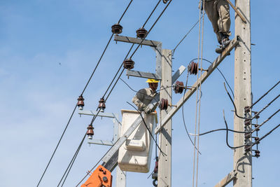 Low angle view of man working on electricity pylon against sky
