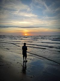 Rear view of boy standing at beach during sunset