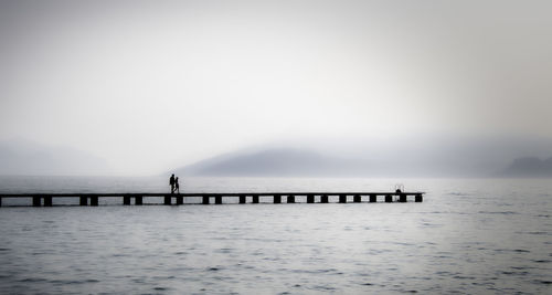 Silhouette people standing on sea against clear sky