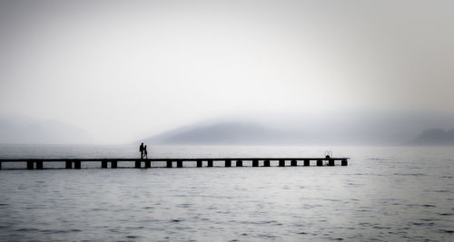 Silhouette people walking on pier over lake during foggy weather