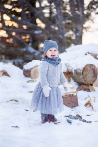 Portrait of happy girl standing on snow covered field during sunset