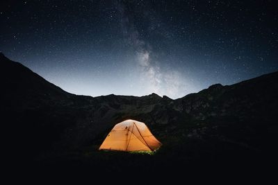 Tent on land against mountains at night