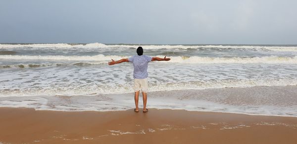 Rear view of man standing on beach against sky