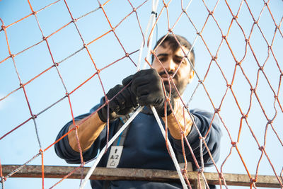 Portrait of woman on chainlink fence against sky