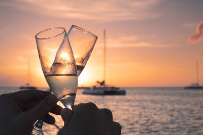 Close-up of hand holding wine glass against sunset sky