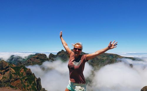 Excited woman with arms outstretched standing on cliff against clear sky