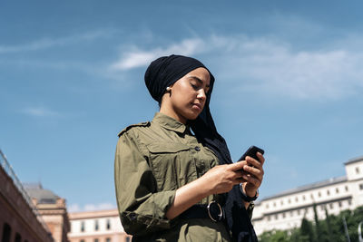 Low angle view of young woman using mobile phone against sky