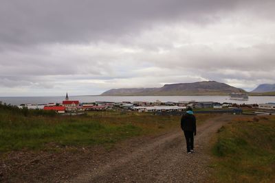 Rear view of man walking on road against sky