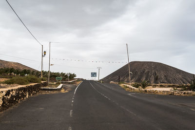 Empty country road against cloudy sky