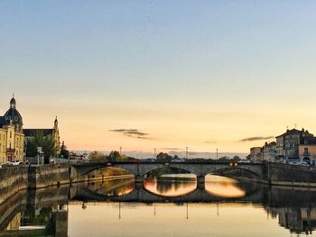 Bridge over river in city against sky during sunset