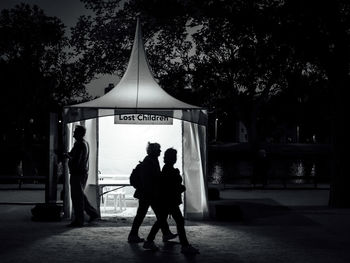 Silhouette women walking by illuminated tent in park at night