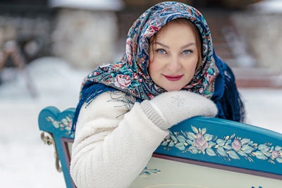 A slavic woman in a national colored scarf, a fur coat and warm mittens sits on a  sleigh. winter