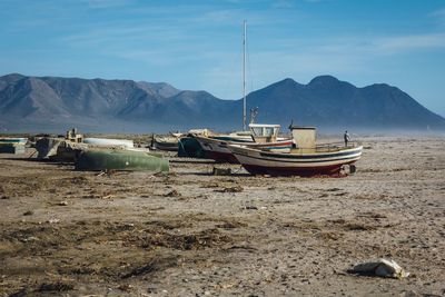 Abandoned boats at beach by mountain against sky