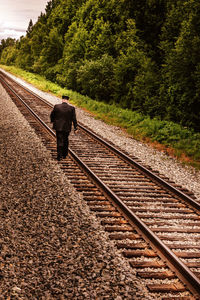 Rear view of man wearing suit walking on railroad track