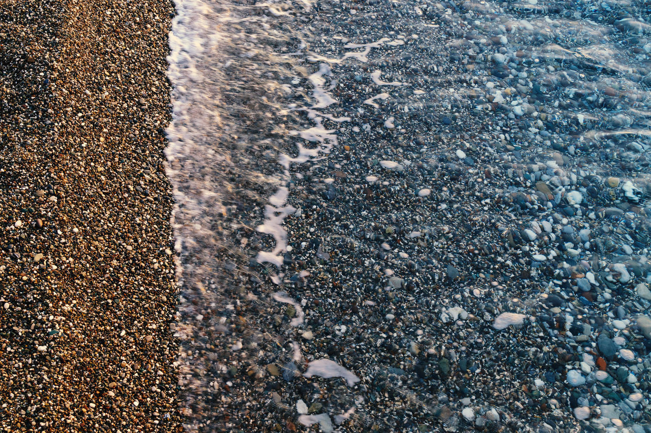 HIGH ANGLE VIEW OF STONES ON WET BEACH