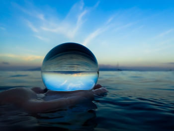 Person hand in sea against sky