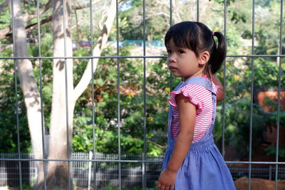 Girl standing by fence against trees