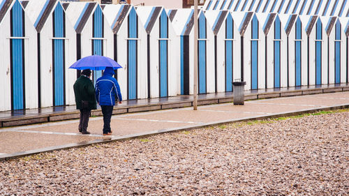 Full length of people sharing umbrella while walking on footpath