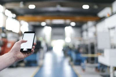 Hand holding laptop with blank screen in a factory workshop