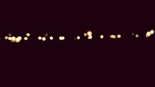 Defocused image of illuminated lights against sky at night