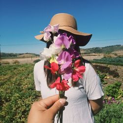 Cropped hand holding flower against woman standing on land