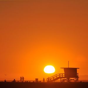 Silhouette lifeguard hut on beach by clear sky during sunset