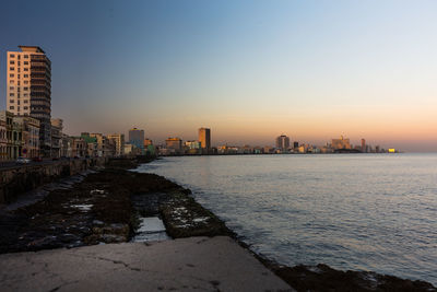 Sea by buildings against clear sky during sunset