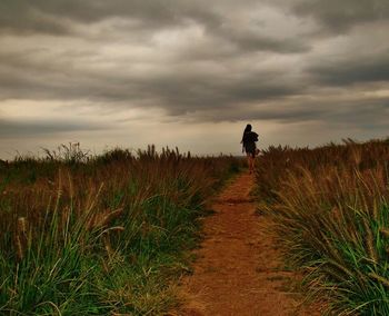 Rear view of man standing on field against cloudy sky