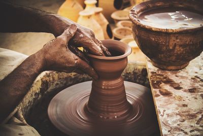 Cropped image of hands making earthen pots on wheel at workshop