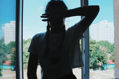 Woman covering face while standing by window