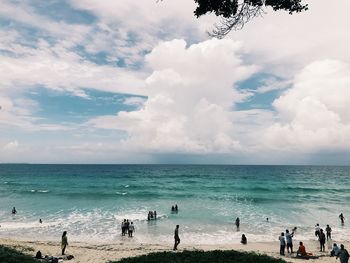 People at beach against cloudy sky