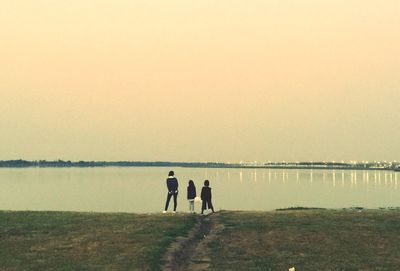 People standing by lake against clear sky