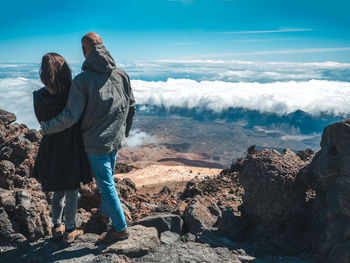 Rear view of people standing on rock against sky