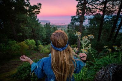 Rear view of woman standing by trees against sky