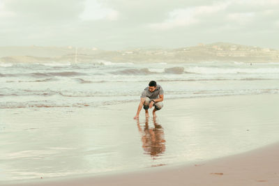 Mid adult man crouching at beach against sky