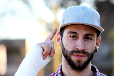 Close-up portrait of young man wearing cap gesturing while standing outdoors