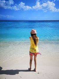 Rear view of girl standing at beach against sky