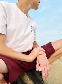 Low section of man sitting against sky